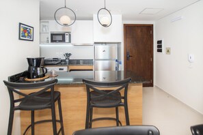 Una cocina moderna con una isla central, dos taburetes de bar, microondas, refrigerador e iluminación colgante.