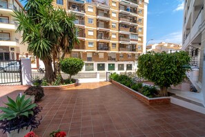 A residential building with multiple balconies, a tiled patio area with plants, and a clear sky. - Apartment in Nerja Near Scenic Beaches (Nerja)