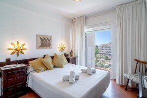 A hotel room with a large bed, two bedside tables, a nightstand, a chair, a balcony with a view, and decorative wall art. - Apartment in Nerja Near Scenic Beaches (Nerja)