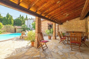 Un patio al aire libre con suelo de piedra, mobiliario de madera y plantas en macetas.