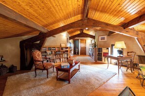 Un loft espacioso con altos techos de madera, una zona de estar acogedora con una silla y una mesa, y una biblioteca repleta de libros.