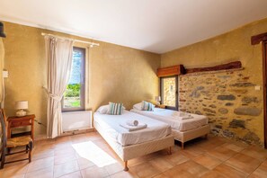 A bedroom with two beds, a stone wall, a wooden cabinet, and a view of greenery outside. - Grand Mas catalan avec piscine, 12 personnes (Ille-sur-Têt)