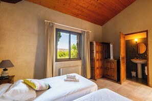 Un dormitorio con dos camas, una ventana con cortinas, un radiador, un armario y un baño con lavamanos y espejo.