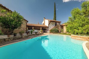 A swimming pool with a stone border, surrounded by potted plants and outdoor furniture. - Grand Mas catalan avec piscine, 12 personnes (Ille-sur-Têt)