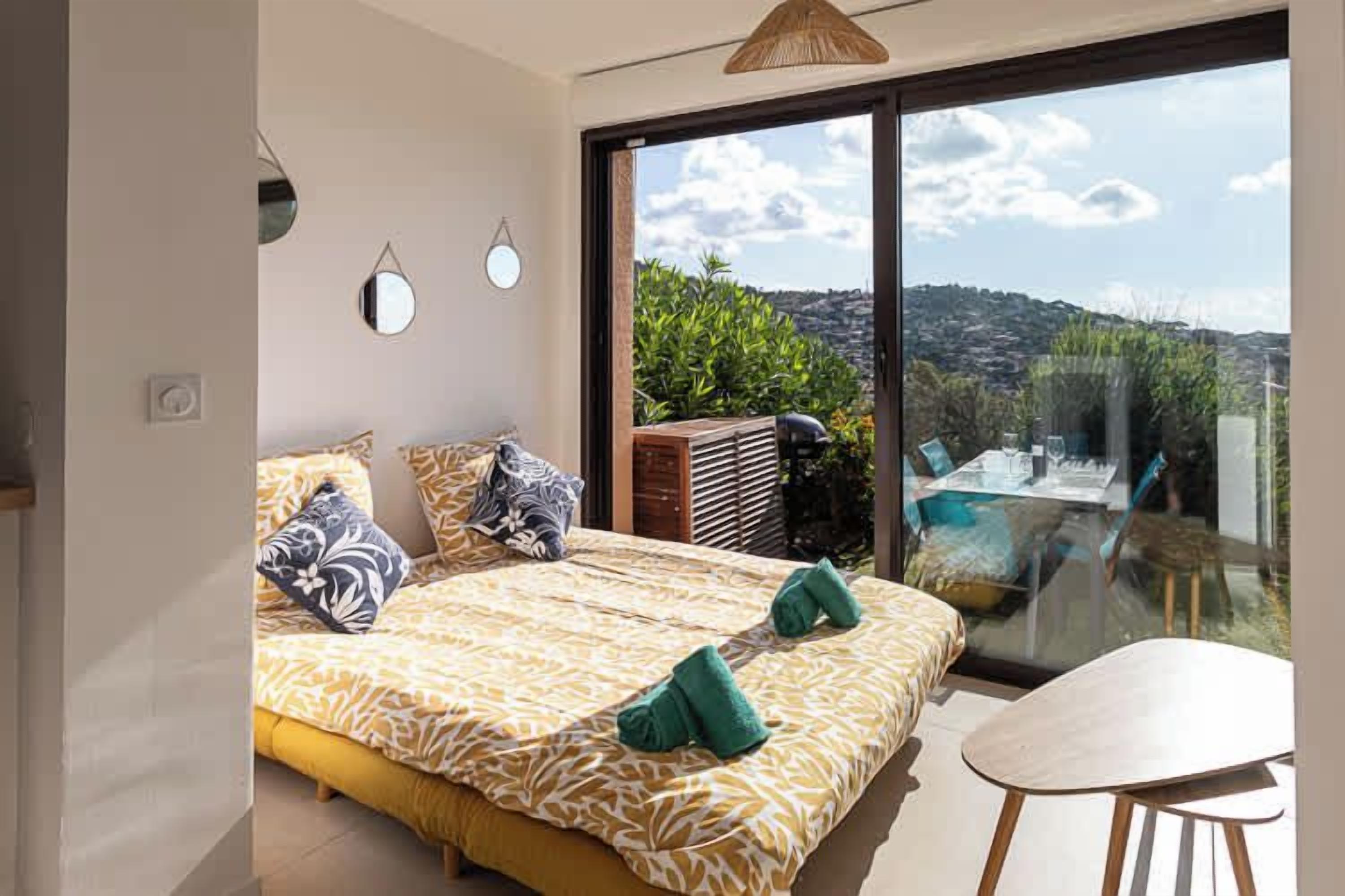 Une chambre avec un grand lit, un balcon avec une table et des chaises, et une vue sur l’extérieur.