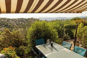 Ein Essbereich im Freien mit Tisch und Stühlen, umgeben von Grünpflanzen und mit Blick auf eine schöne Landschaft.
