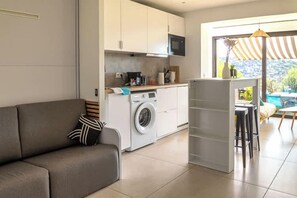 A modern living space with a sofa, a washing machine, and a dining area with a view. - Cala Bianca - Cocon familial vue mer, 6 personnes (Bormes-les-Mimosas)