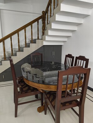 Un coin repas comprenant une table ronde, six chaises et un escalier avec des balustres en bois.