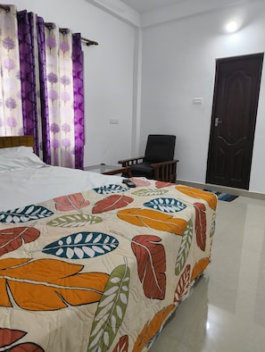 A hotel room with a bed, a chair, a door, and curtains.