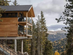 Eine mehrstöckige Holzhütte mit Balkonen, eingebettet in eine bewaldete Berglandschaft.