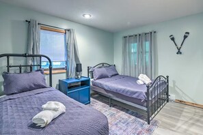 A bedroom with two beds, a nightstand, a window with curtains, and a wall-mounted paddleboard. - Pocono Cabin w/ Fire Pit, Kayaks & Lake Access (Big Bass Lake)