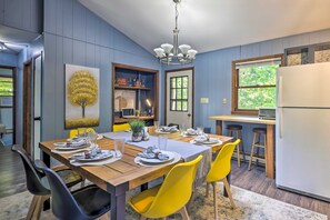 Un coin repas avec une table en bois dressée pour quatre personnes, des chaises jaunes et un lustre moderne.