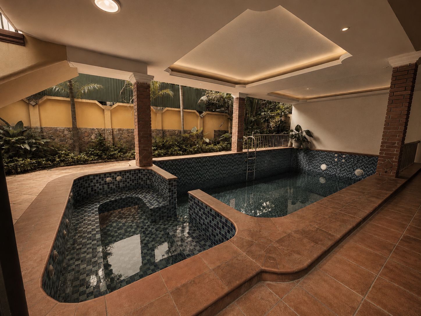 Un espace bien-être comprenant un jacuzzi et une piscine séparée, le tout entouré d’une terrasse carrelée et d’un mur en briques.