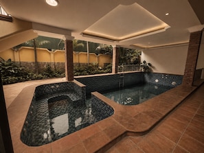 Un área de spa con hidromasaje y piscina separada, rodeada por una terraza con baldosas y un muro de ladrillo.