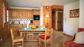 A wooden kitchen with a dining table set for breakfast, a clock on the wall, and a painting on the wall.