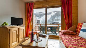 A cozy room with a bed, a television on a wooden cabinet, and a window with curtains.