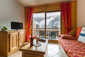 A cozy room with a bed, a television on a wooden cabinet, and a window with curtains. - Mountain Retreat With Heated Pool (Saint-Chaffrey)