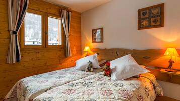 A cozy wooden room with a bed, two bedside lamps, a window with curtains, and a wall-mounted picture.