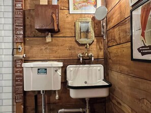 A wooden bathroom with a white toilet, a white sink with a black rim, and a mirror above the sink. - Remarkable Boultons Barn With hot tub and opt Sauna (Newton Abbot)