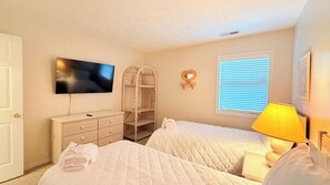 Ein Schlafzimmer mit zwei Betten, einem Fernseher, einer Lampe, einem Kleiderschrank und einem Fenster mit Jalousien.