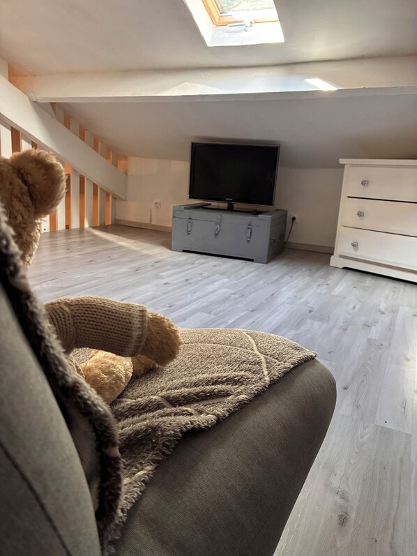 Une pièce confortable avec un canapé, un téléviseur posé sur une commode et une lucarne.