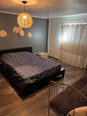 A bedroom with a bed, a bedside table, a chair, a hanging light fixture, and a window with curtains. - Family home in Tarascon in the countryside: walks, relaxation, and a warm, friendly atmosphere  (Tarascon)