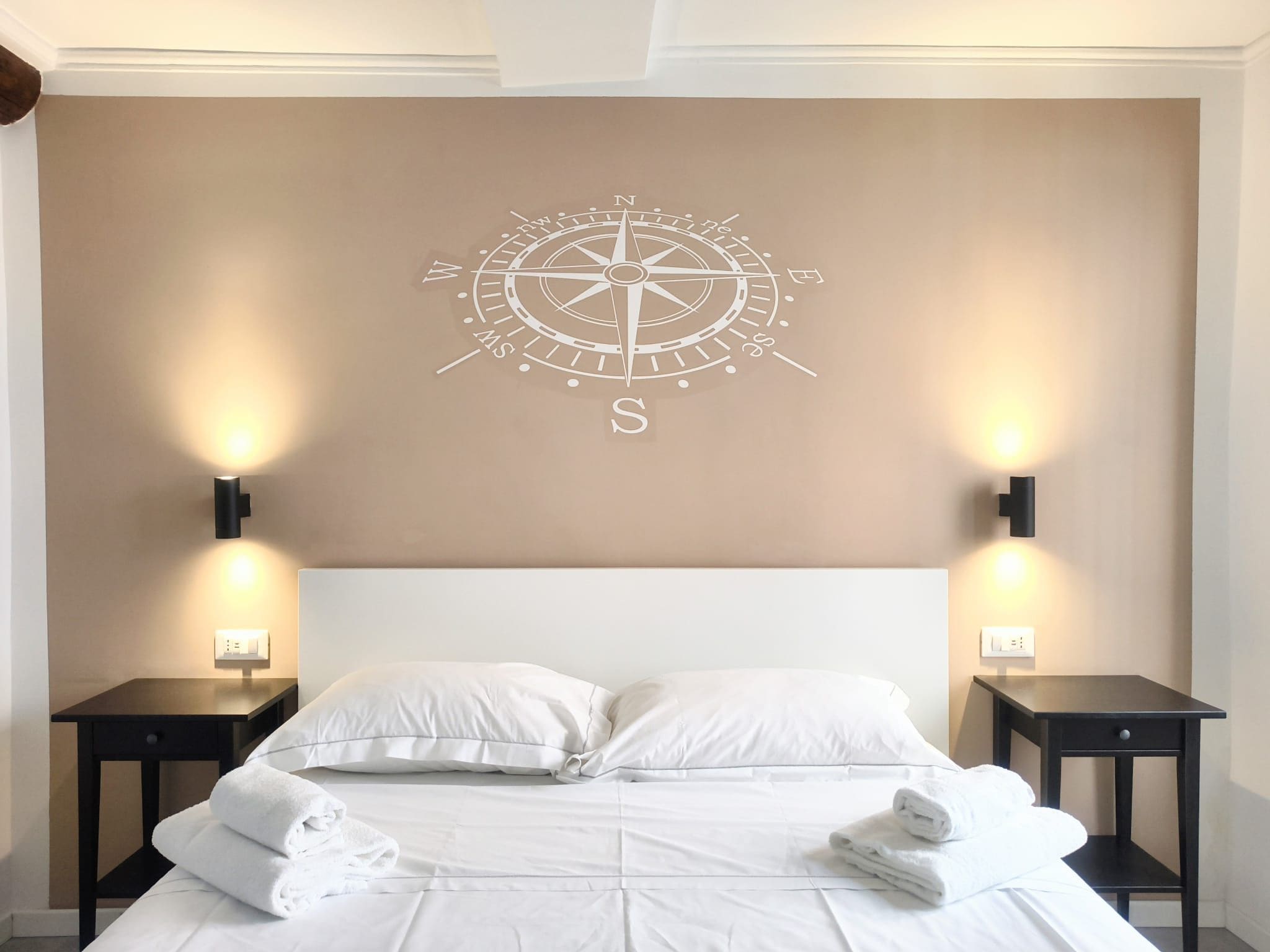 A hotel room with a bed, white bedding, two bedside tables with lamps, and a compass wall art.
