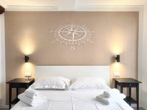 A hotel room with a bed, white bedding, two bedside tables with lamps, and a compass wall art. - Casa dei Fregoso | Cozy apartment, 5 minutes from the aquarium (Genova)