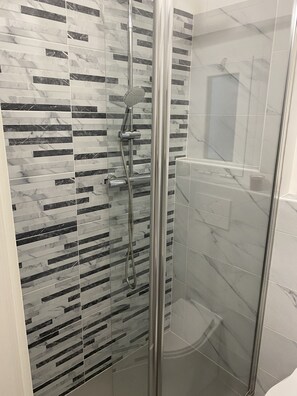 A shower with a glass door, a handheld showerhead, and a wall with a marble pattern. - Casa dei Fregoso | Cozy apartment, 5 minutes from the aquarium (Genova)