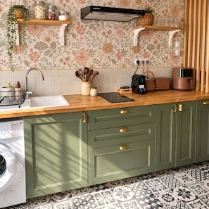 A kitchen with a washing machine, a sink, a countertop with a coffee maker, and a patterned backsplash.