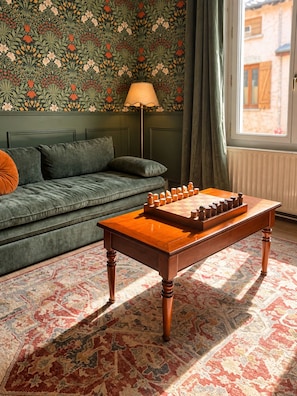 A room with a sofa, a wooden table with a checkered game, and a patterned carpet.