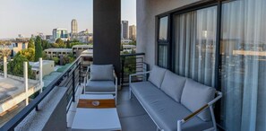 Varanda com sofá, cadeiras e mesa, com vista para a paisagem urbana.