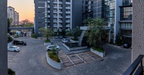 A modern building complex with multiple parking spaces, a landscaped area with trees, and a clear sky. - Imperial Ventures Apartments - 1 BR apt (Sandton)