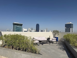 Terrassa al terrat amb mobles d'exterior, un skyline urbà al fons i un cel serè.