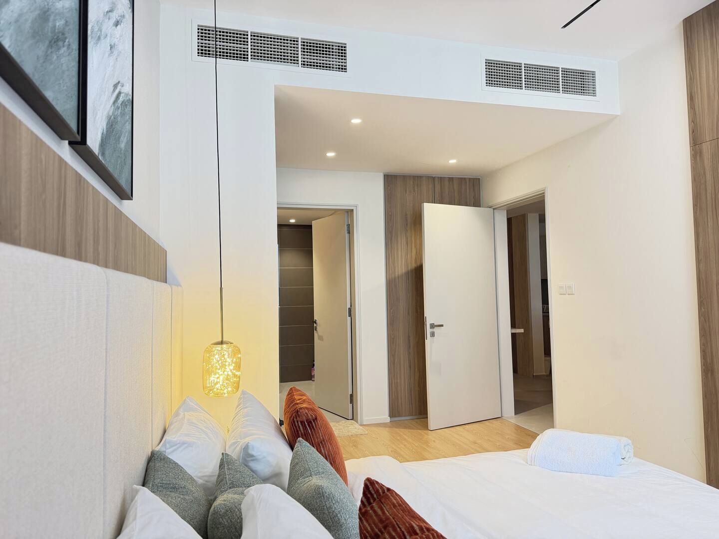 A modern bedroom with a bed, a hanging light fixture, and a door leading to another room.