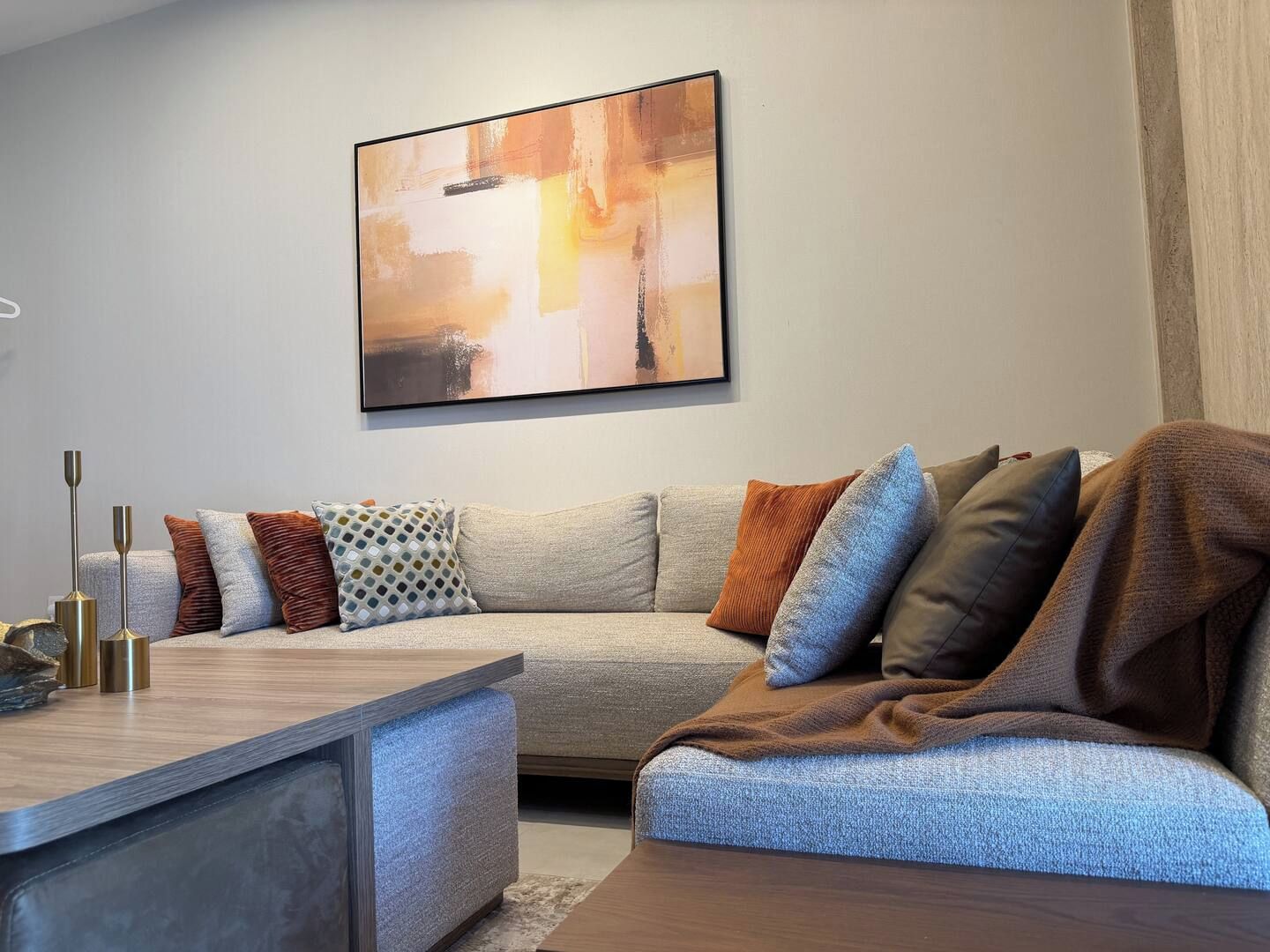 A modern living room with a sectional sofa, a coffee table, and a large abstract painting on the wall.