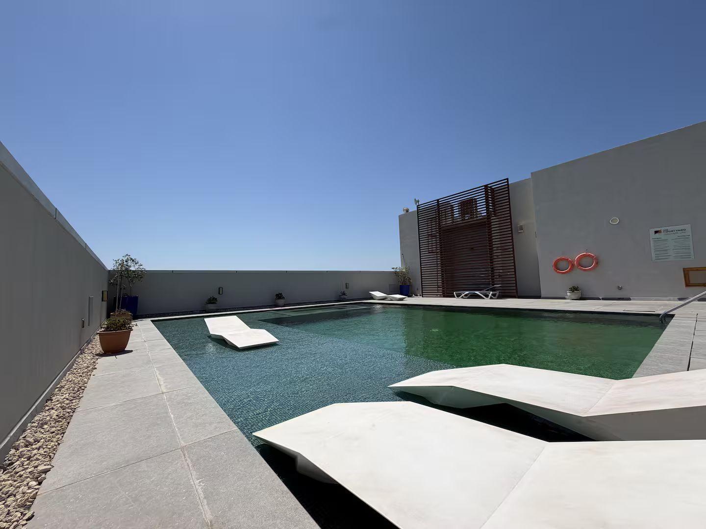 A modern outdoor swimming pool with clear blue water, surrounded by a low wall and a flat roof.