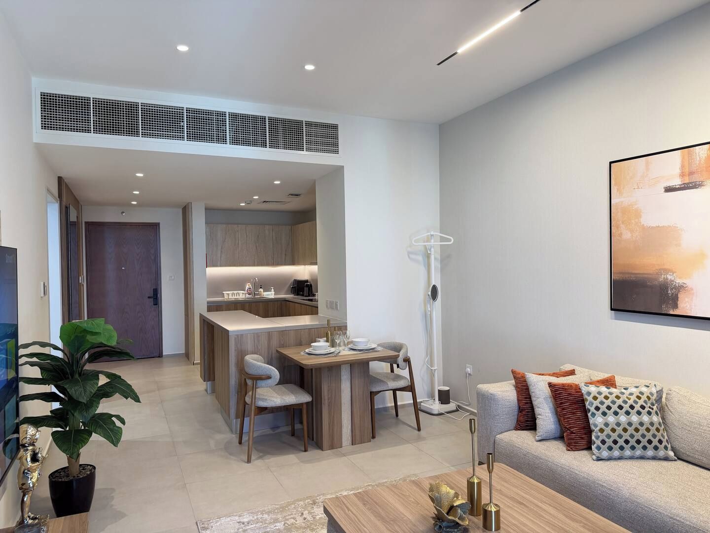 A modern living room with a sofa, a dining area with chairs, a kitchen in the background, and a large window.