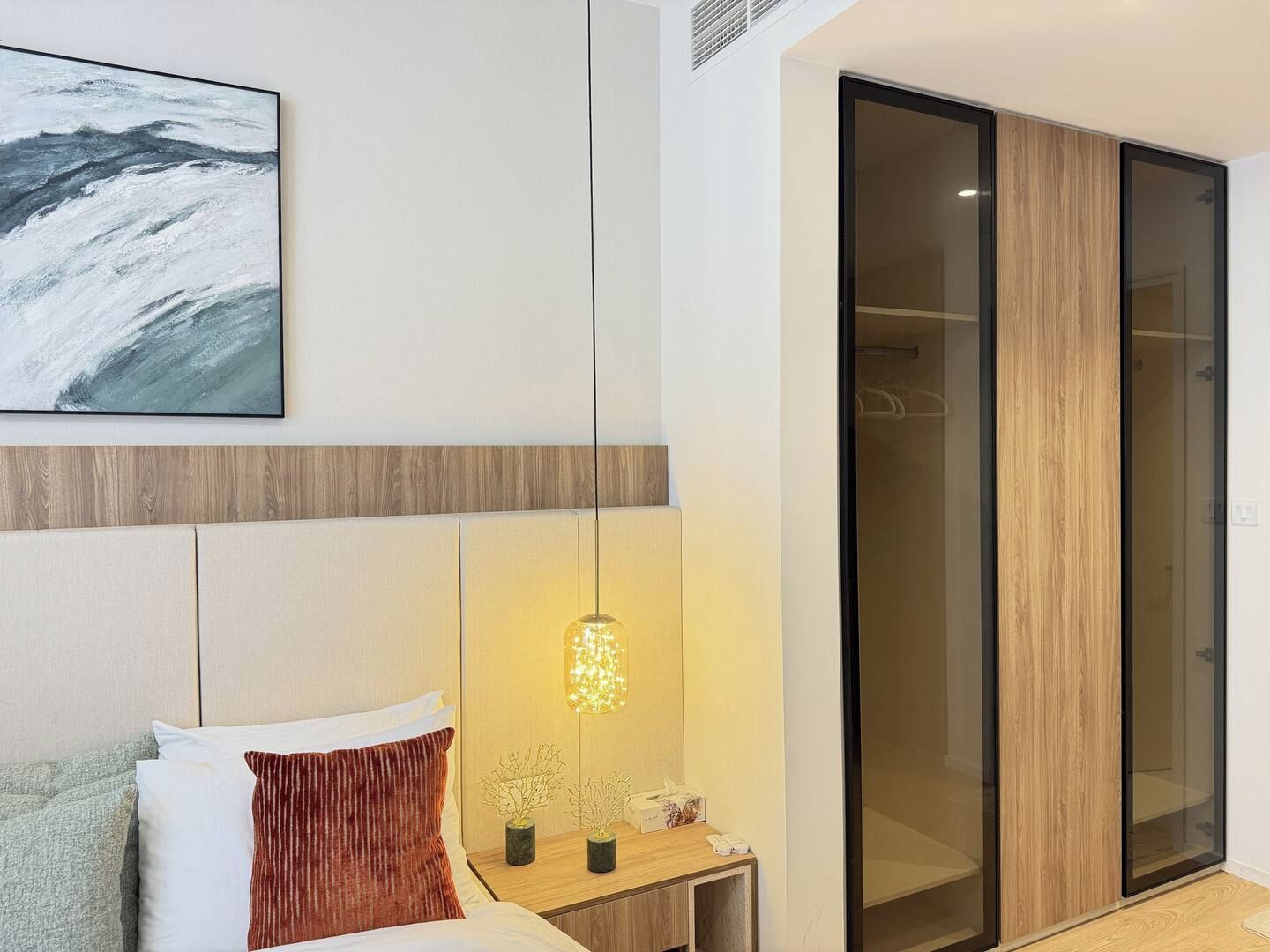 A modern hotel room with a bed, bedside table, lamp, and a sliding glass door closet.