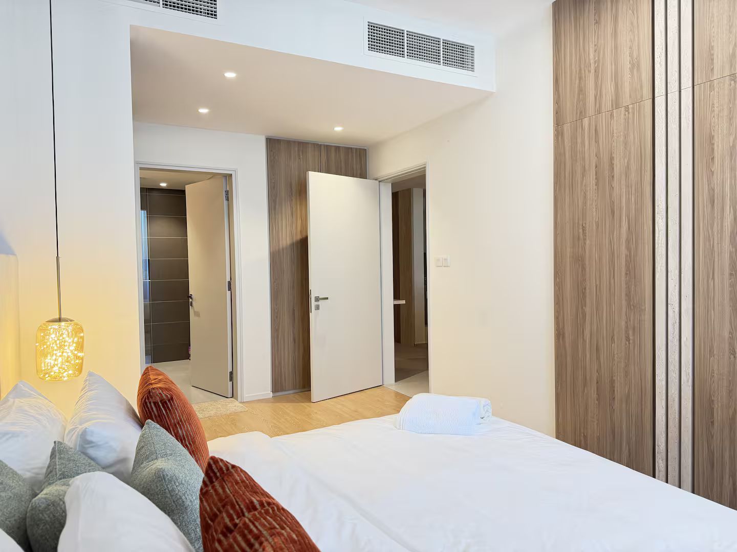 A hotel room with a bed, a bedside lamp, a wardrobe, and a door leading to another room.