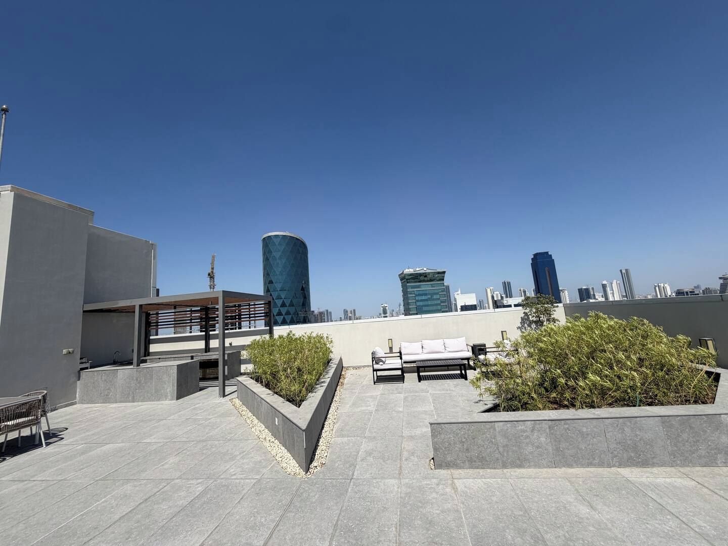 A rooftop terrace with seating areas, planters, and a clear view of the city skyline.
