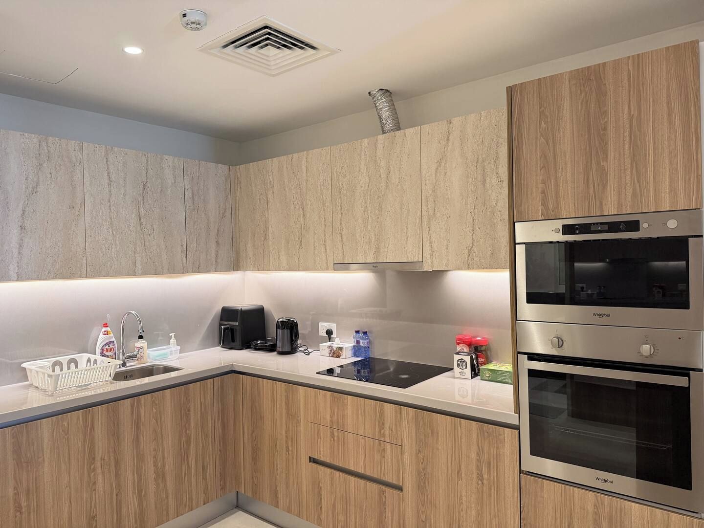 A modern kitchen with wooden cabinets, a built-in oven, and a countertop with various appliances and items.