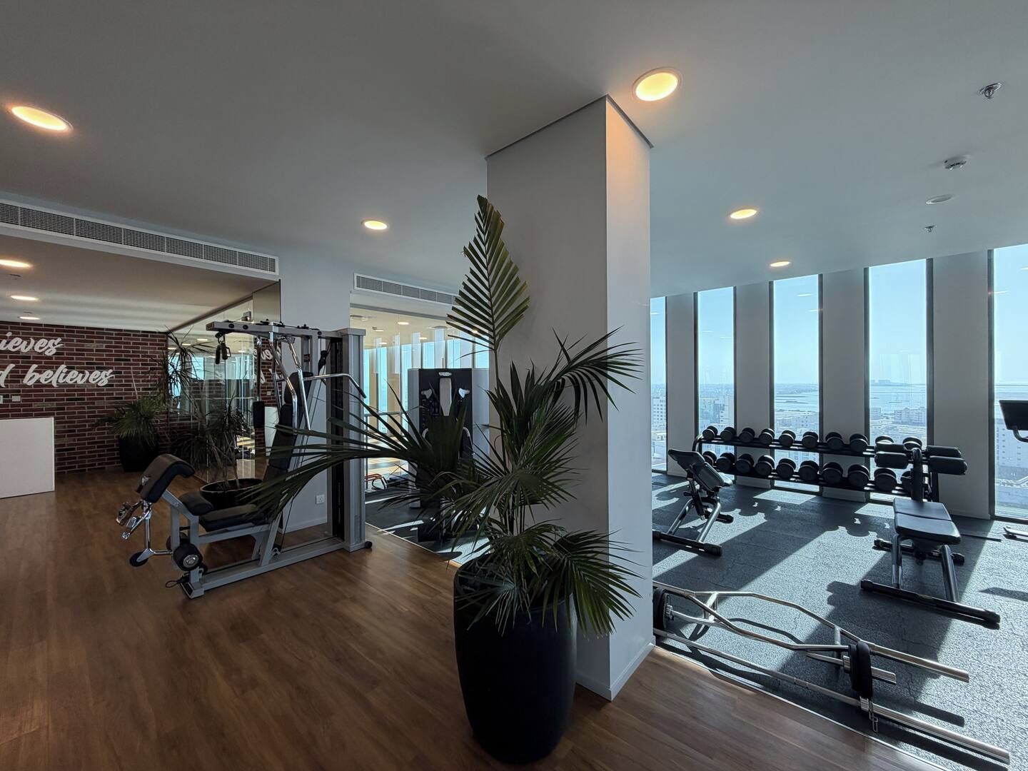 Et moderne fitnesscenter med træningsudstyr, store vinduer og et motiverende citat på væggen.