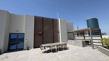 An outdoor patio area with a table and chairs, a basketball hoop, and a building with a modern design.