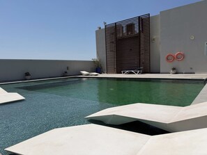 Una piscina en la azotea con diseño moderno, que incluye formas geométricas y una fuente de agua azul cristalina.