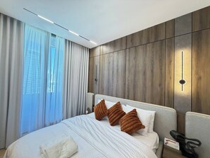 Habitación de hotel moderna con una cama grande, una mesita de noche con teléfono y vista a la ciudad a través del ventanal.