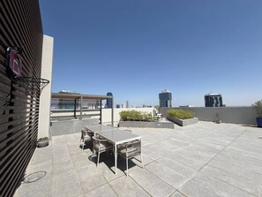Una terraza en la azotea con mesa y sillas, un aro de baloncesto y vistas a un horizonte urbano.