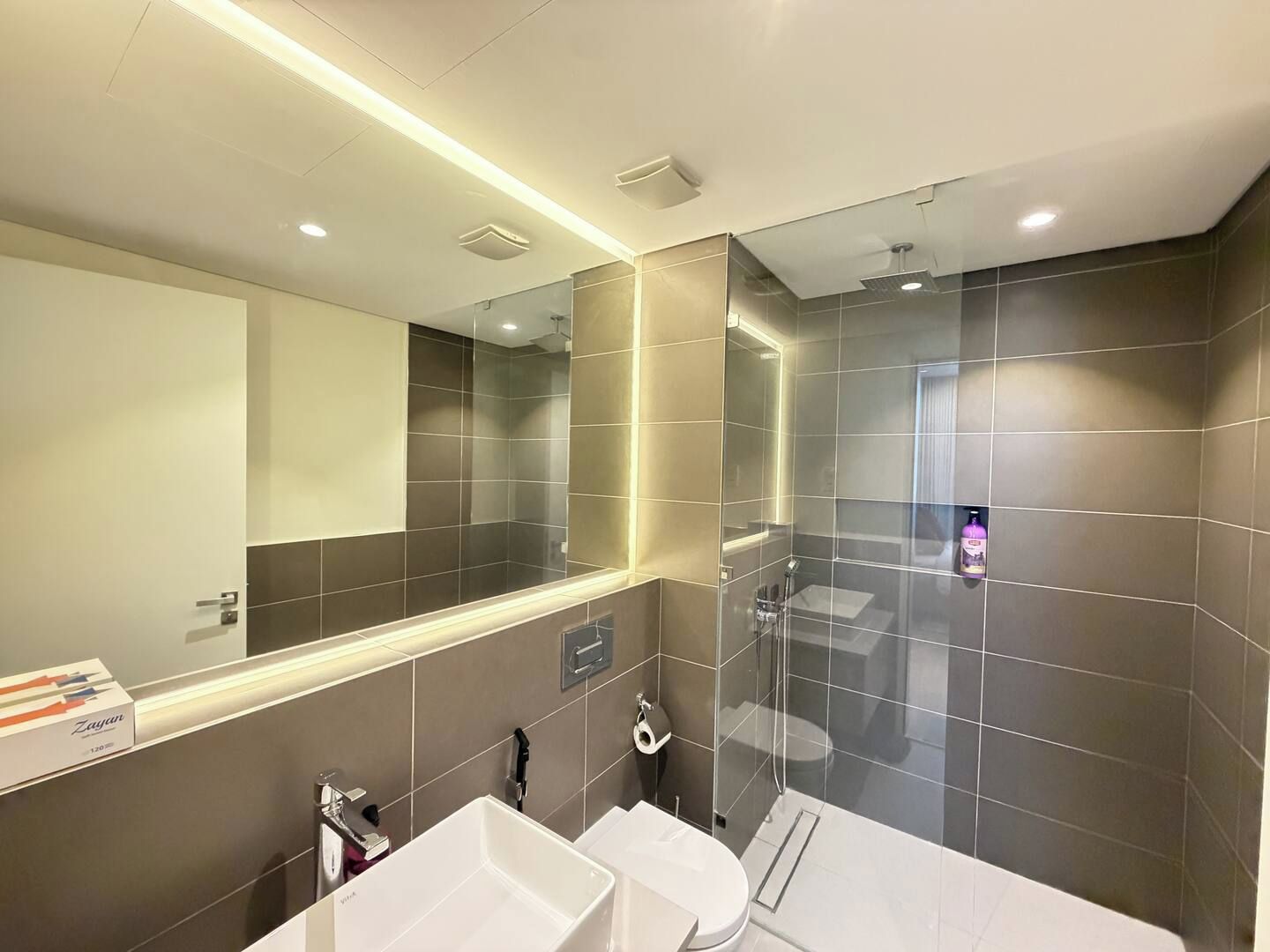 A modern bathroom with a large mirror, two sinks, and a shower area.