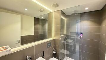 A modern bathroom with a large mirror, two sinks, and a shower area.