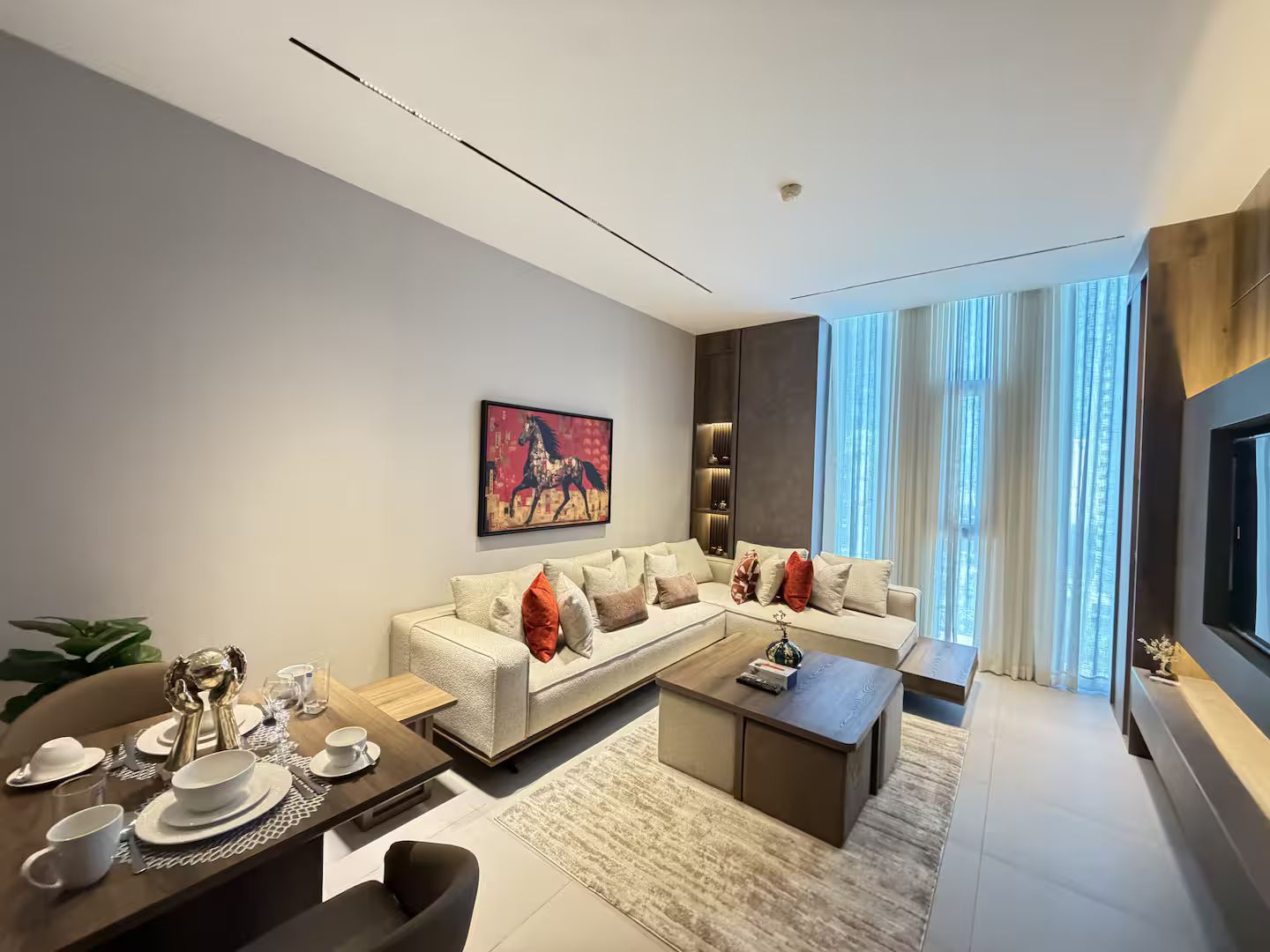 A modern living room with a sectional sofa, a dining area with a table set for two, and a large window with curtains.